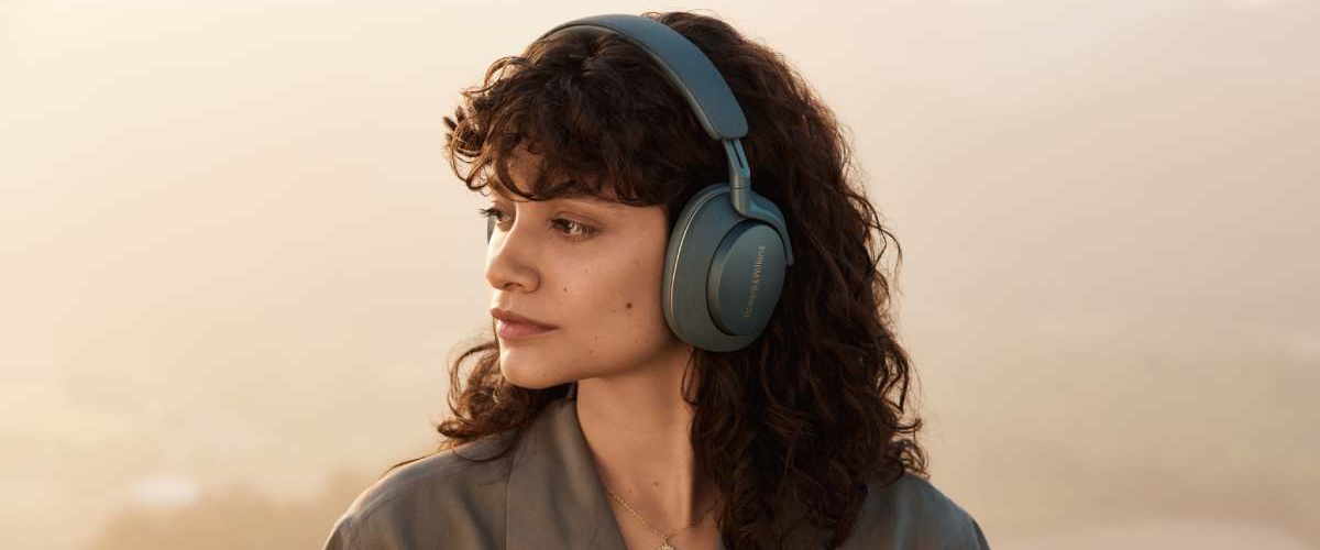 Sieviete valkā zilas Bowers & Wilkins bezvadu austiņas un skatās uz sāniem