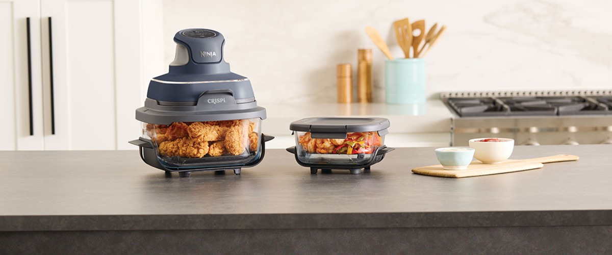 Ninja Crispi pārnēsājams karstā gaisa friteris uz virtuves virsmas ar gatavu ēdienu