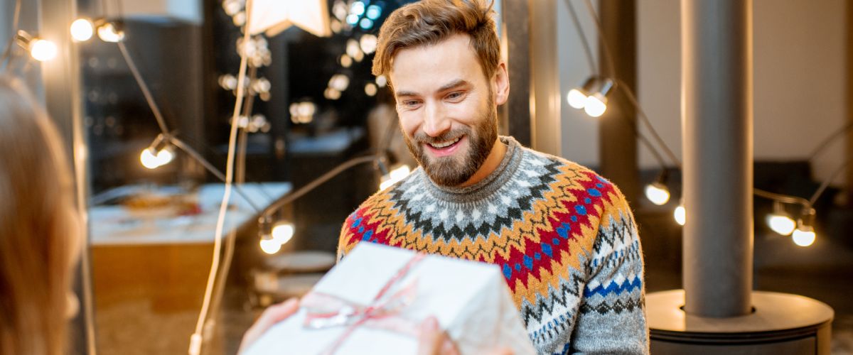 Smaidošs vīrietis saņem iepakotu Ziemassvētku dāvanu