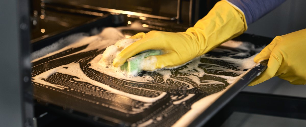 Priekšplānā roka tīra cepeškrāsni ar sūkli un tīrīšanas līdzekli