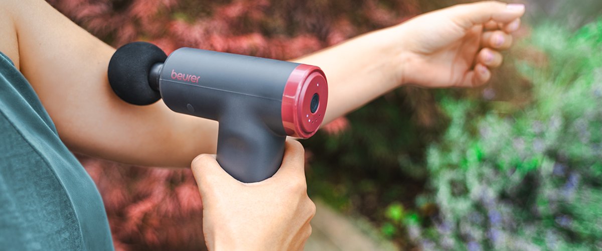 Sieviete tur rokās Beurer masāžas pistoli muskuļu atslābināšanai