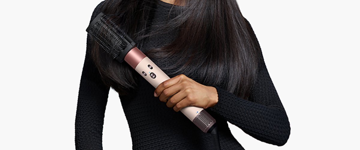 sieviete melnā kleitā tur rokās Dyson Airwrap matu veidošanas ierīci