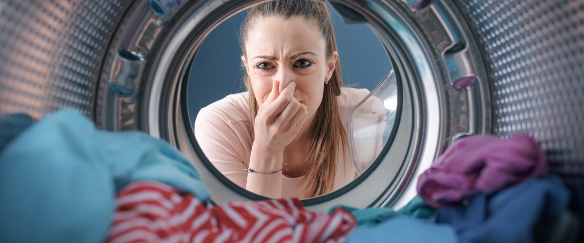 Sieviete skatās veļas mašīnas tvertnē, meklējot nepatīkama aromāta cēloņus