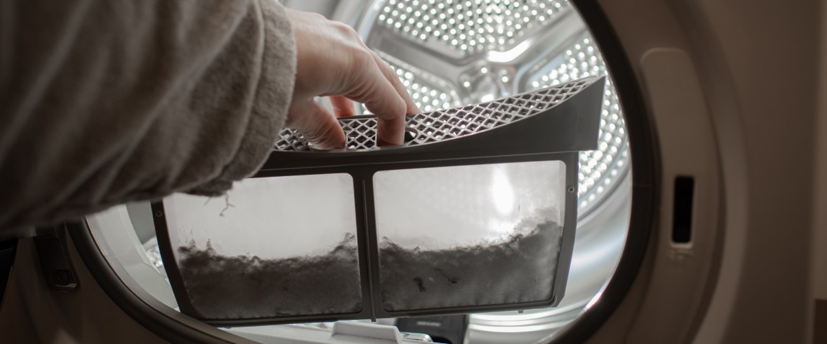 Sievietes roka pie veļas mašīnas tvertnes tur netīru filtru