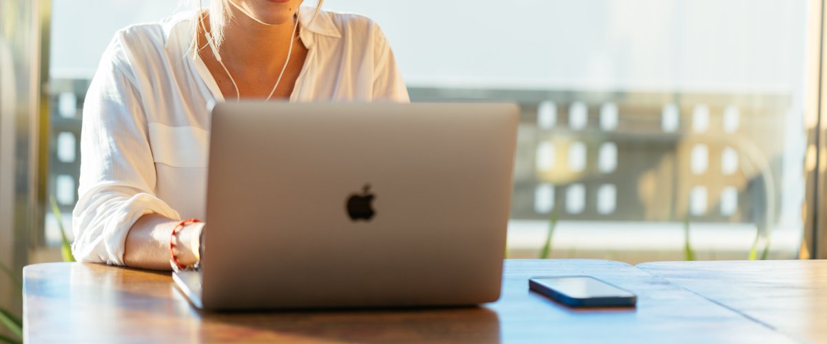 Smaidīga sieviete izmanto MacBook portatīvo datoru gaišā telpā pie galda