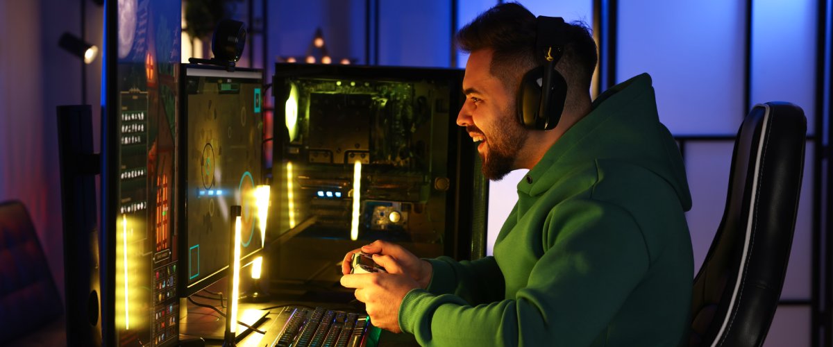 Jauns spēlētājs ar austiņām spēlē pie spēļu datora ar diviem monitoriem